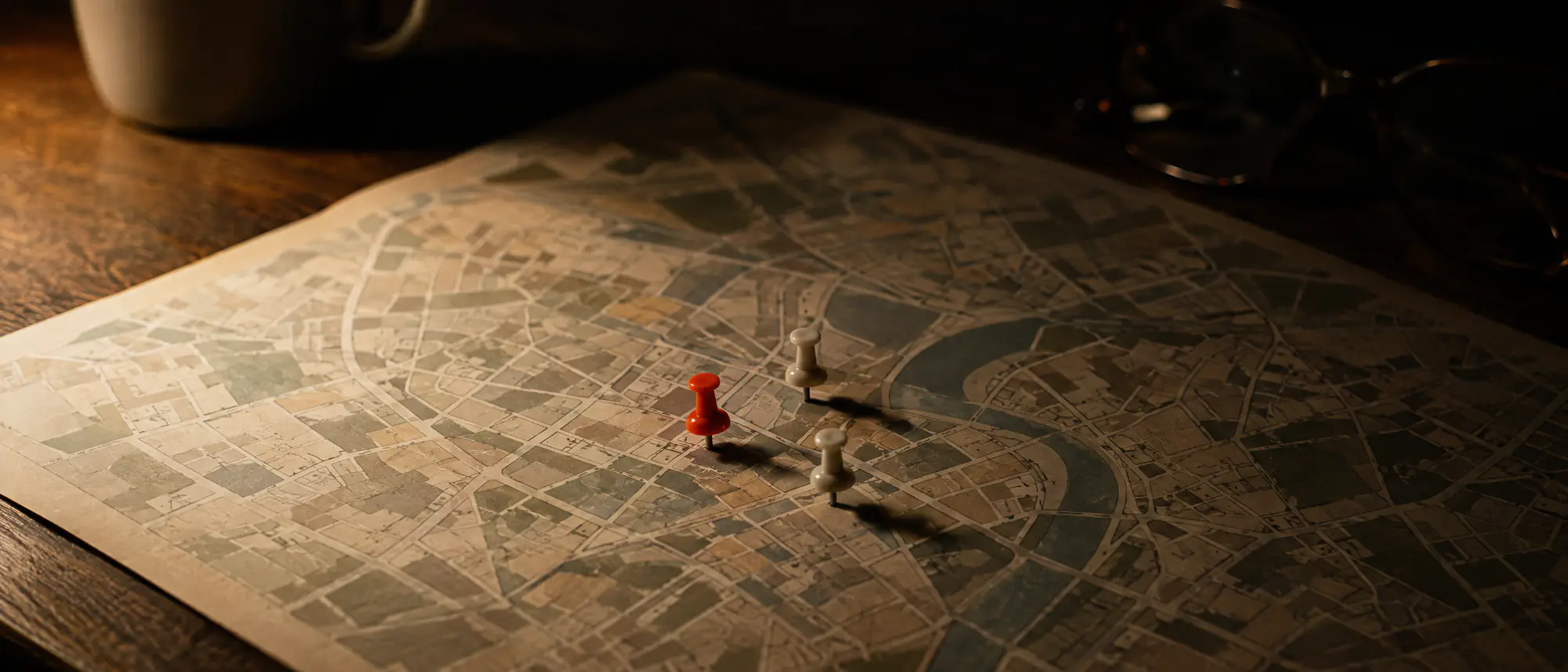 Three pushpins, one orange and two white, clustered on a paper street map under a desk lamp.